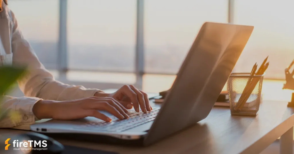 Kobieta siedząca w biurze i pracująca na laptopie w systemie fireTMS. Biuro jest skąpane w promieniach zachodzącego słońca