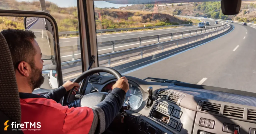 Kierowca siedzący w kabinie ciągnika siodłowego i kierujący zestawem transportowym na autostradzie w słoneczny i suchy dzień