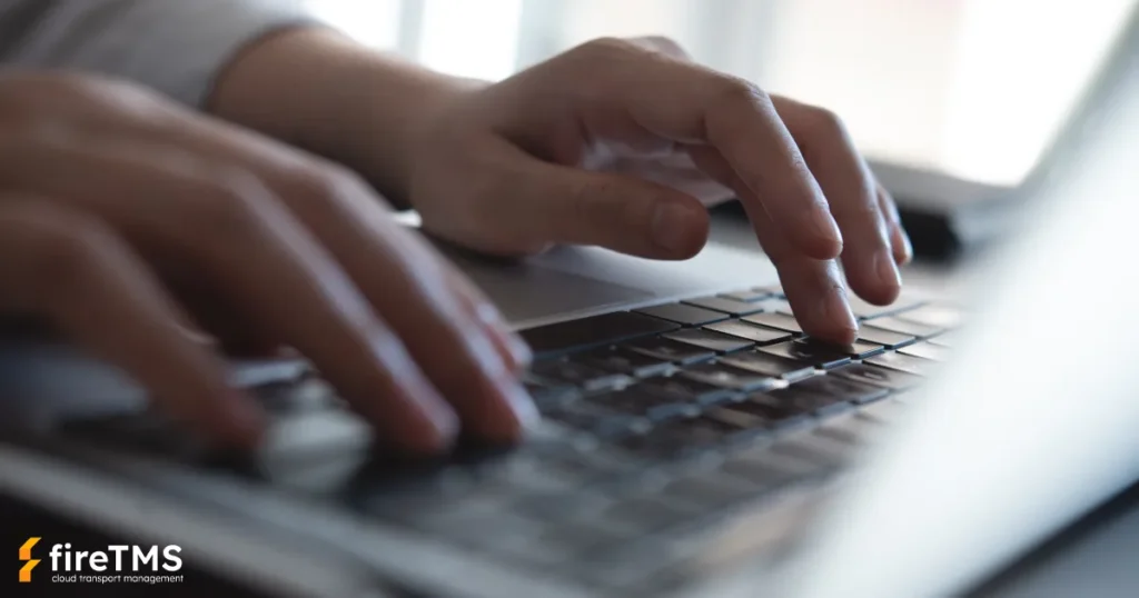 Zbliżenie na dłonie spedytora pracującego na laptopie w biurze nad obsługą zlecenia spedycyjnego