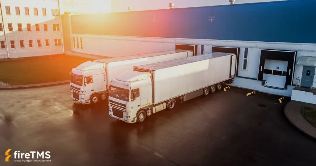 Dwa białe zestawy transportowe stojące przy froncie przeładunkowym w magazynie w słoneczny dzień